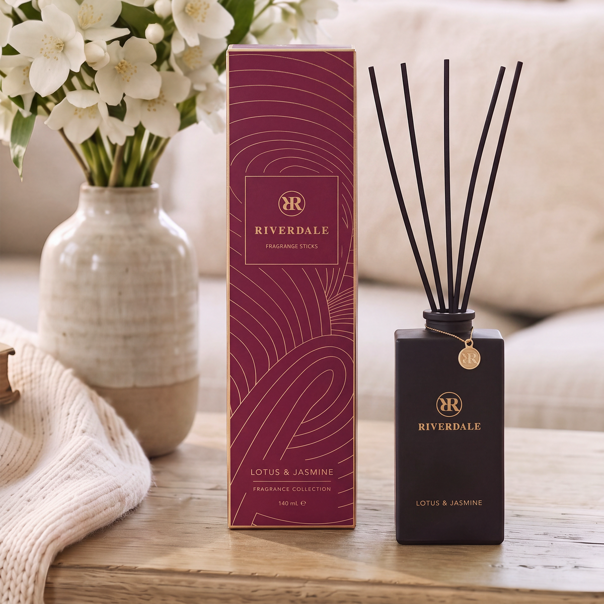 Riverdale Lotus & Jasmine fragrance sticks in a burgundy bottle with gold accents and matching gift box on a table.