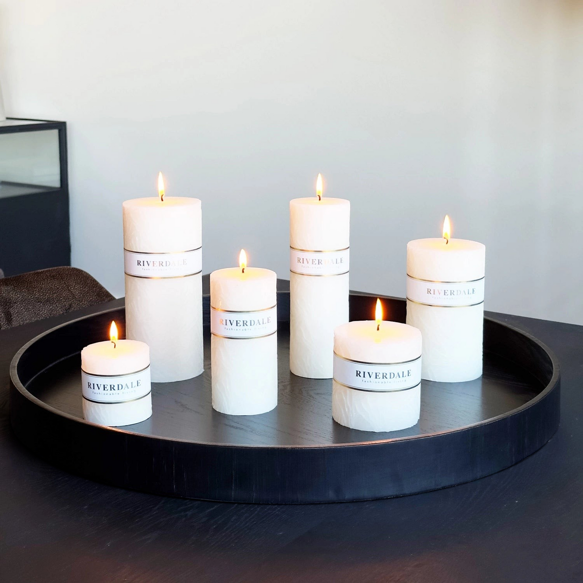 Riverdale white pillar candles with textured wave design and branded paper bands arranged on a black decorative tray.