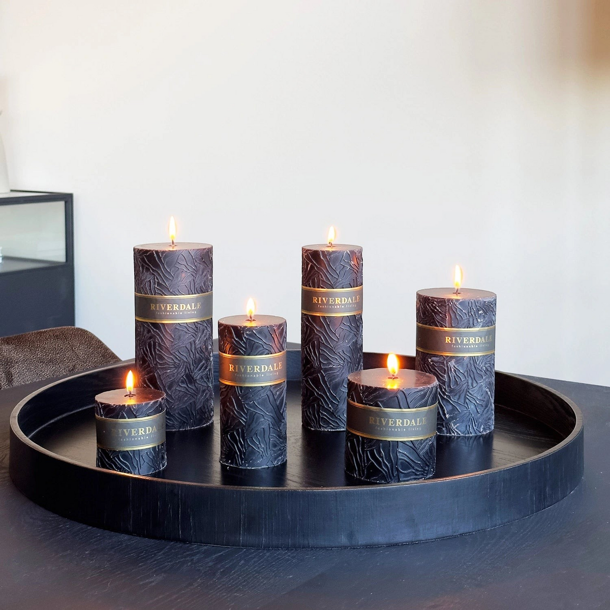 Riverdale Wave black pillar candles with textured surface and gold branding on a round black decorative tray